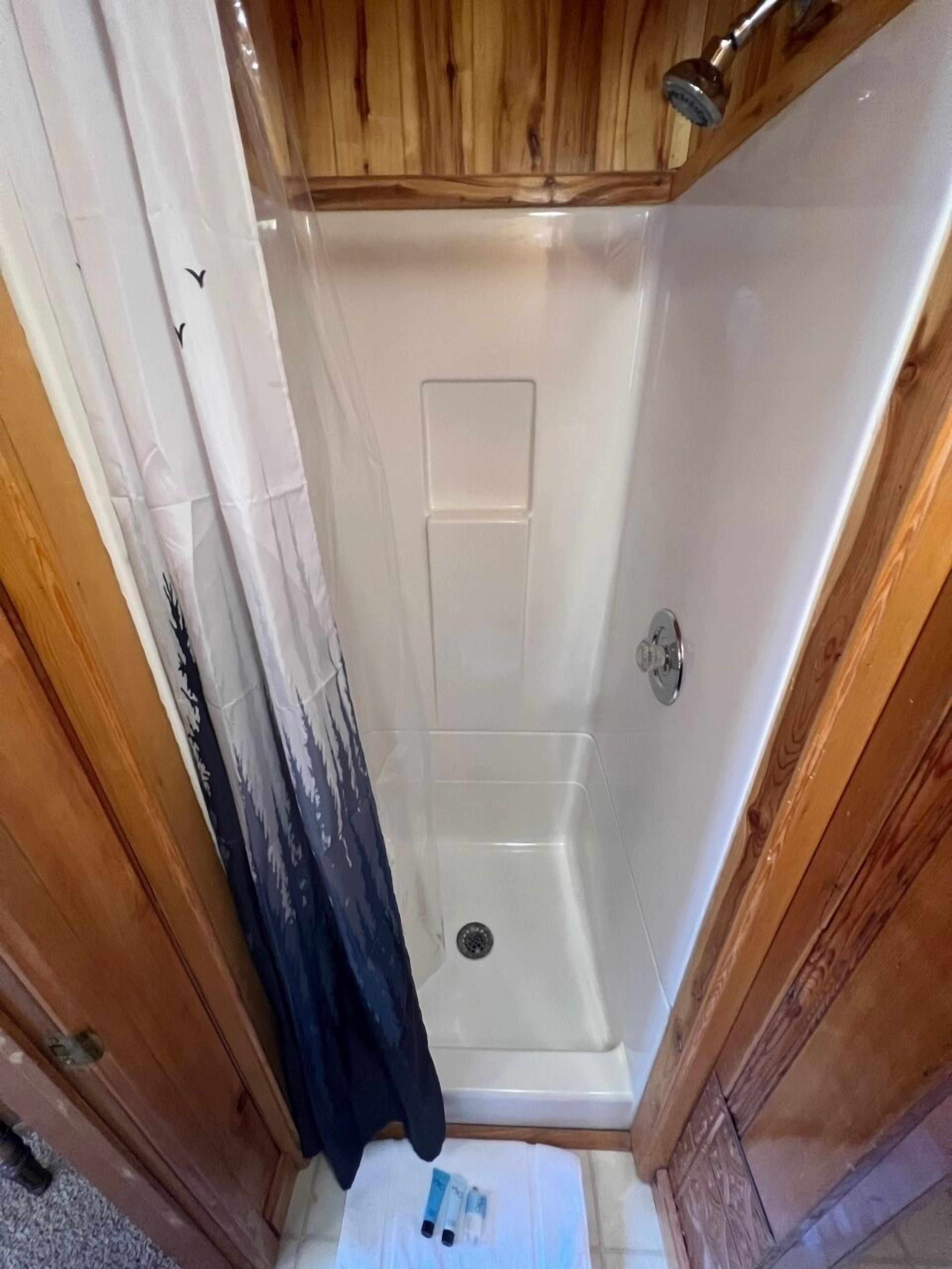 Un área de ducha pequeña y cerrada, con una puerta de madera y un cabezal de ducha.