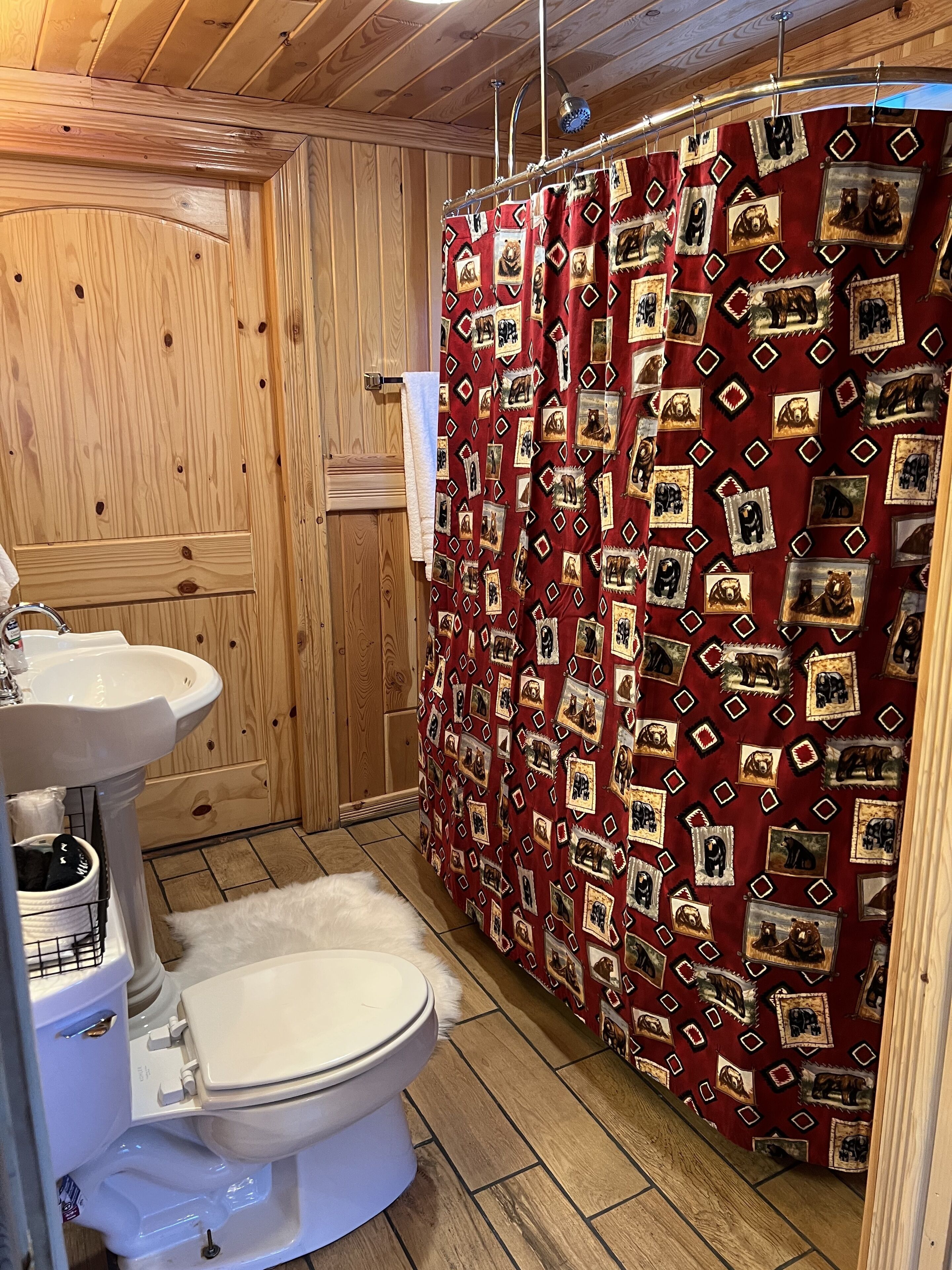 A wooden cabin bathroom with a toilet, sink, and shower curtain featuring bear prints.