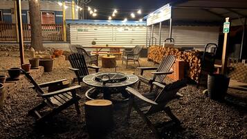 Een terras met een ronde tafel en stoelen, omringd door potplanten en een vuurkuil.