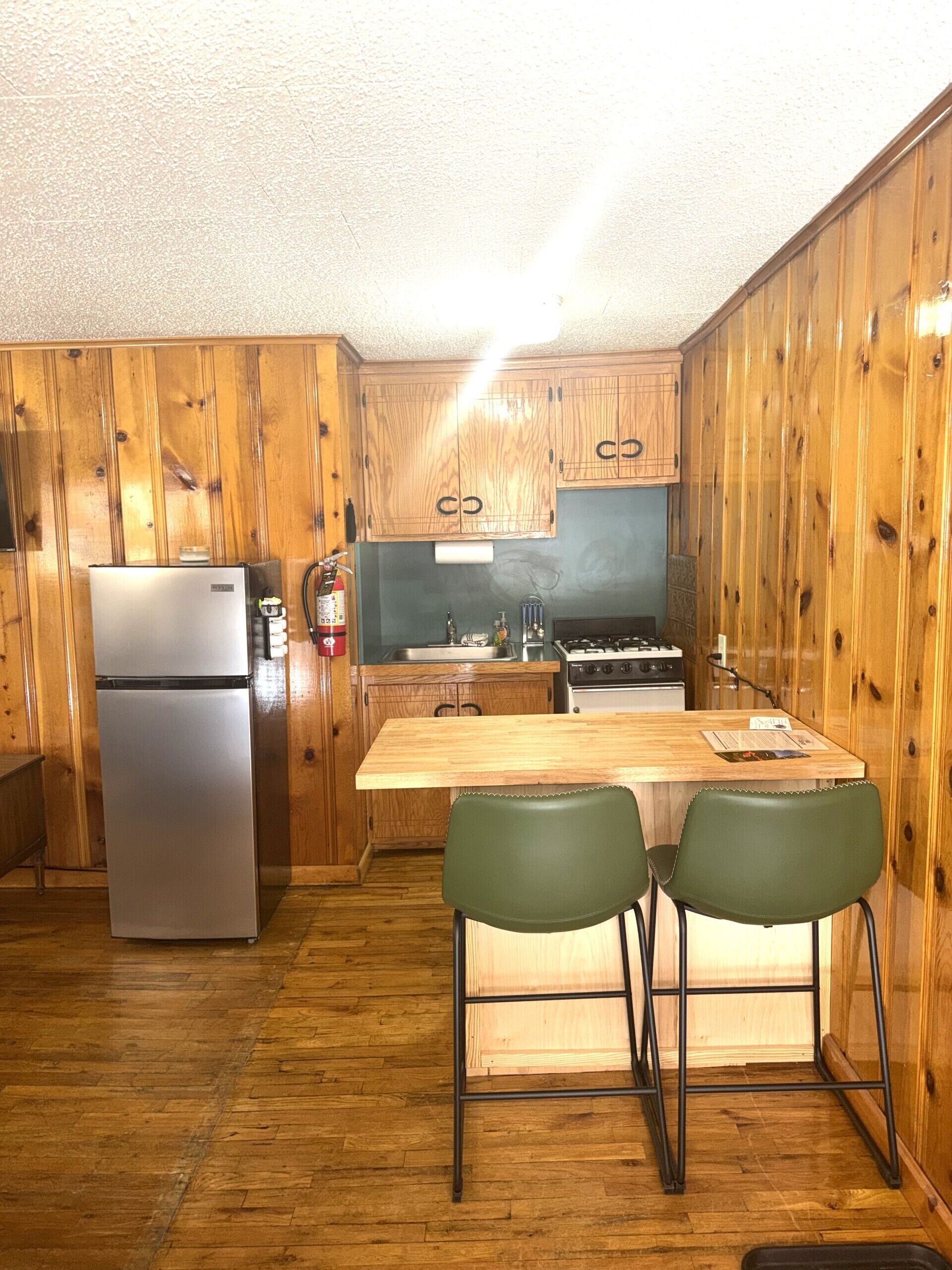 Eine kompakte Küche mit Holzausstattung, einem Kühlschrank, einem Herd und einem Esstisch aus Holz mit zwei Stühlen.
