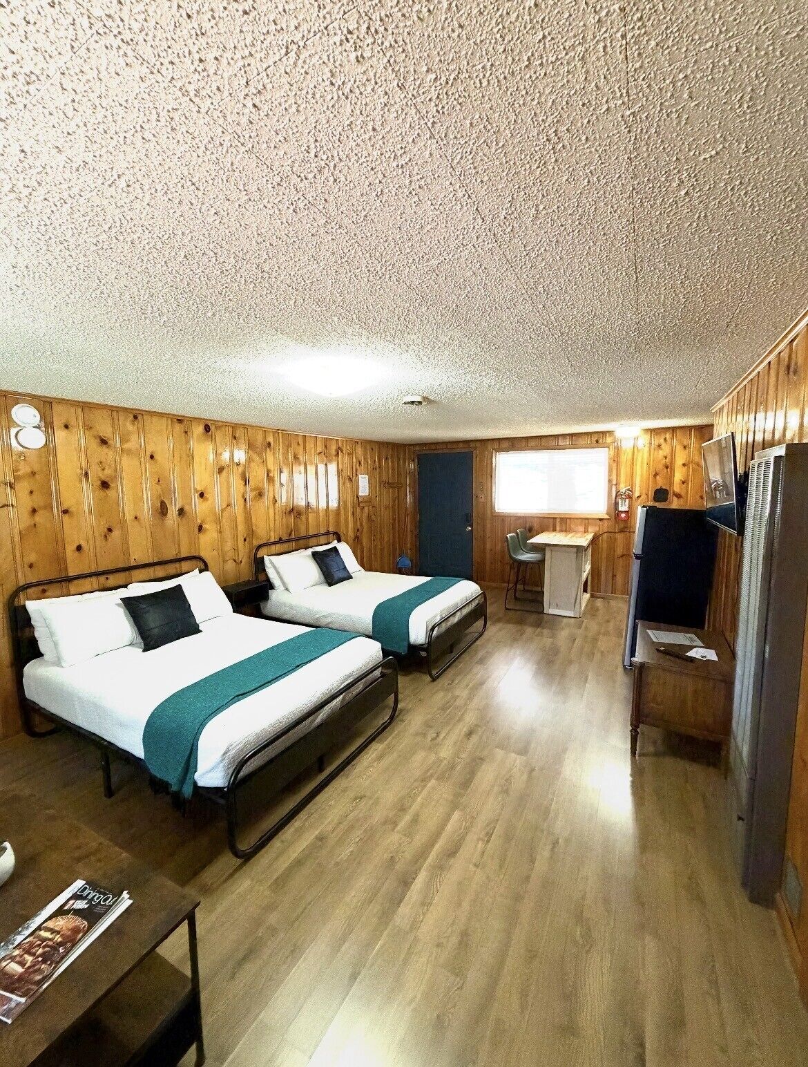Une chambre avec deux lits, une petite table, un téléviseur et une fenêtre.