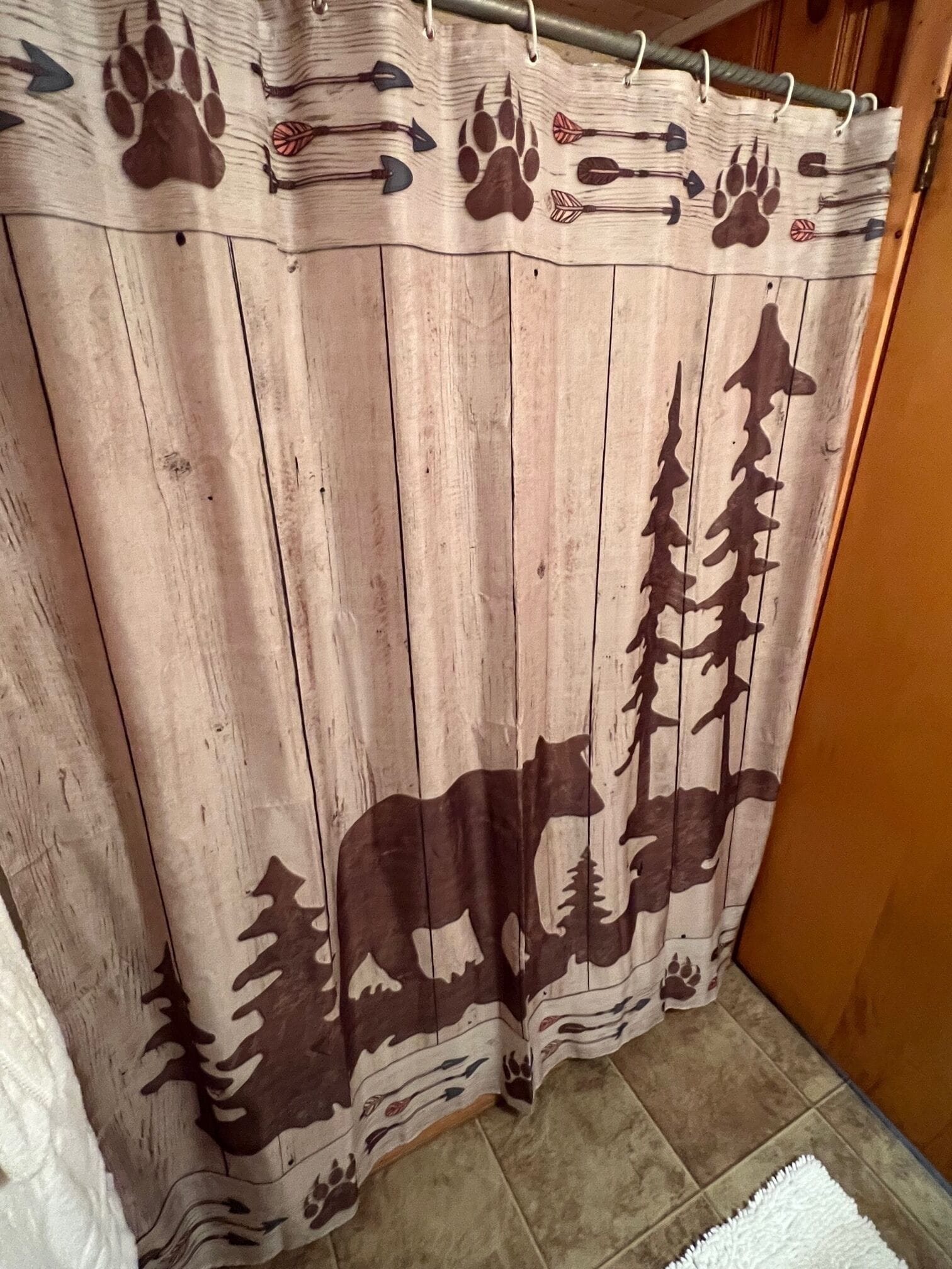 Un rideau orné d’un motif représentant une forêt et un ours, suspendu dans une pièce aux murs en bois et au sol carrelé.