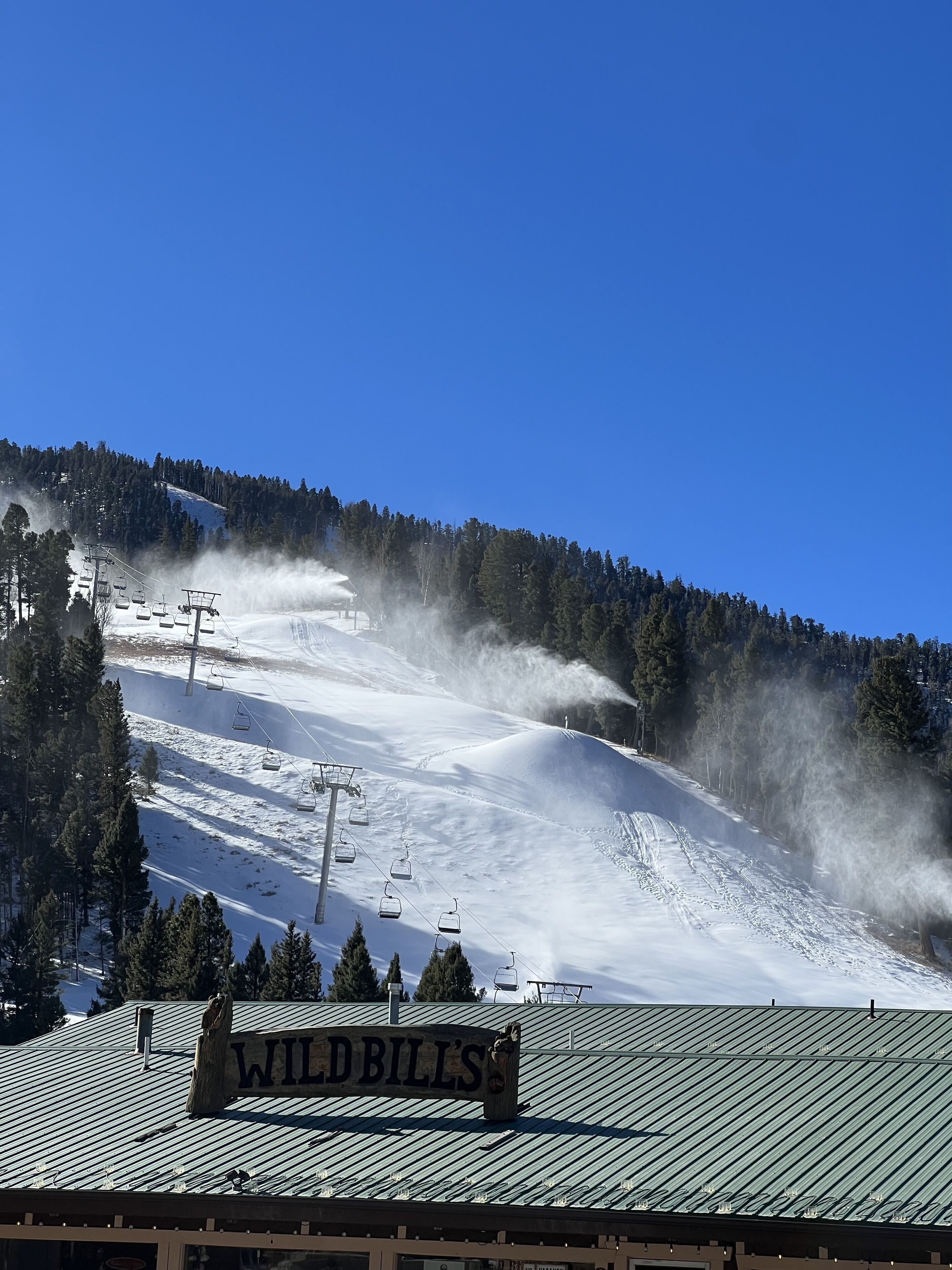 A ski lift on a snowy slope with a sign reading "WILD BILL'S" on a building.