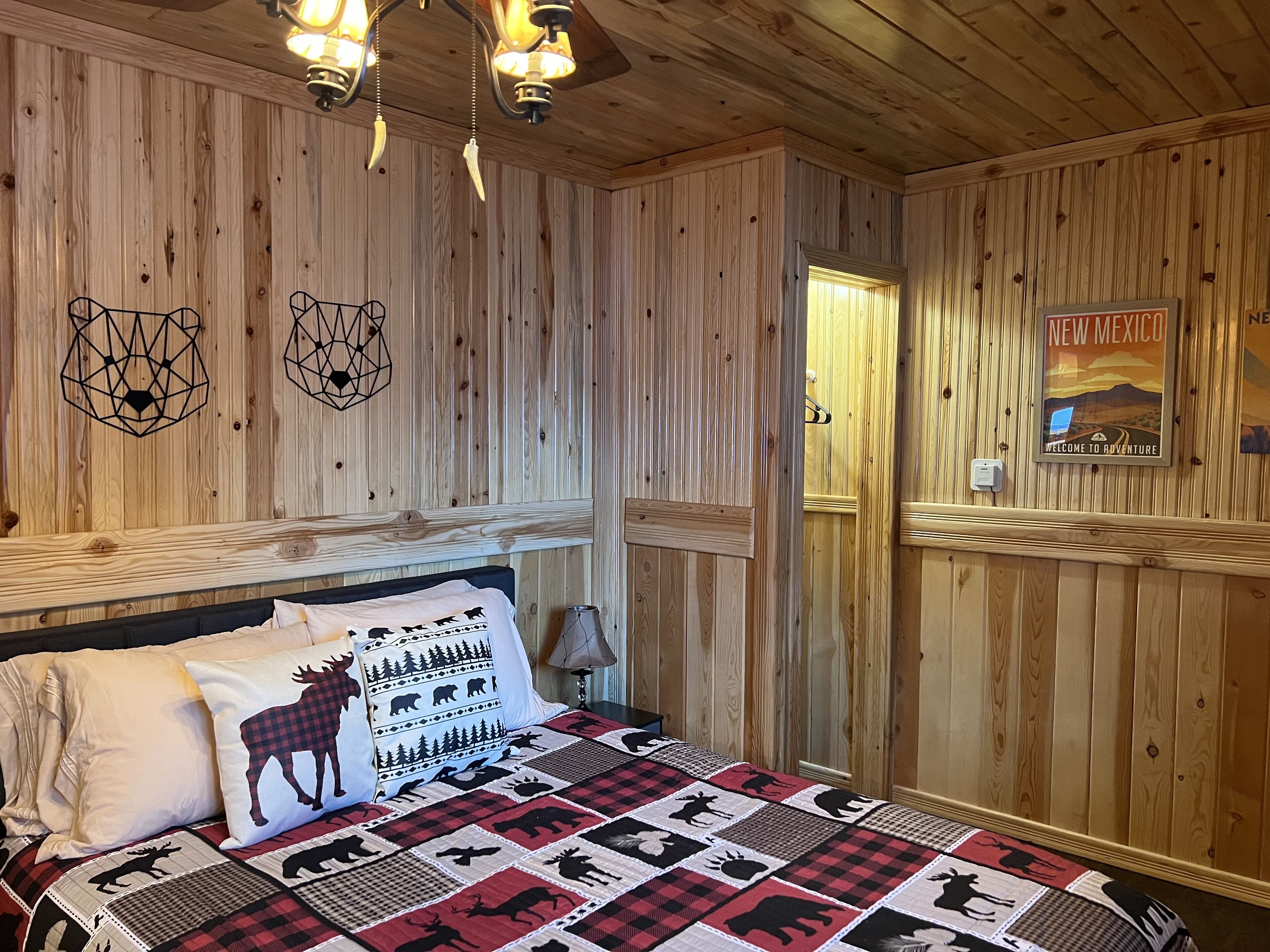 A wooden-paneled room with a bed featuring a quilt with animal prints, a wall-mounted light fixture, and a poster on the wall.