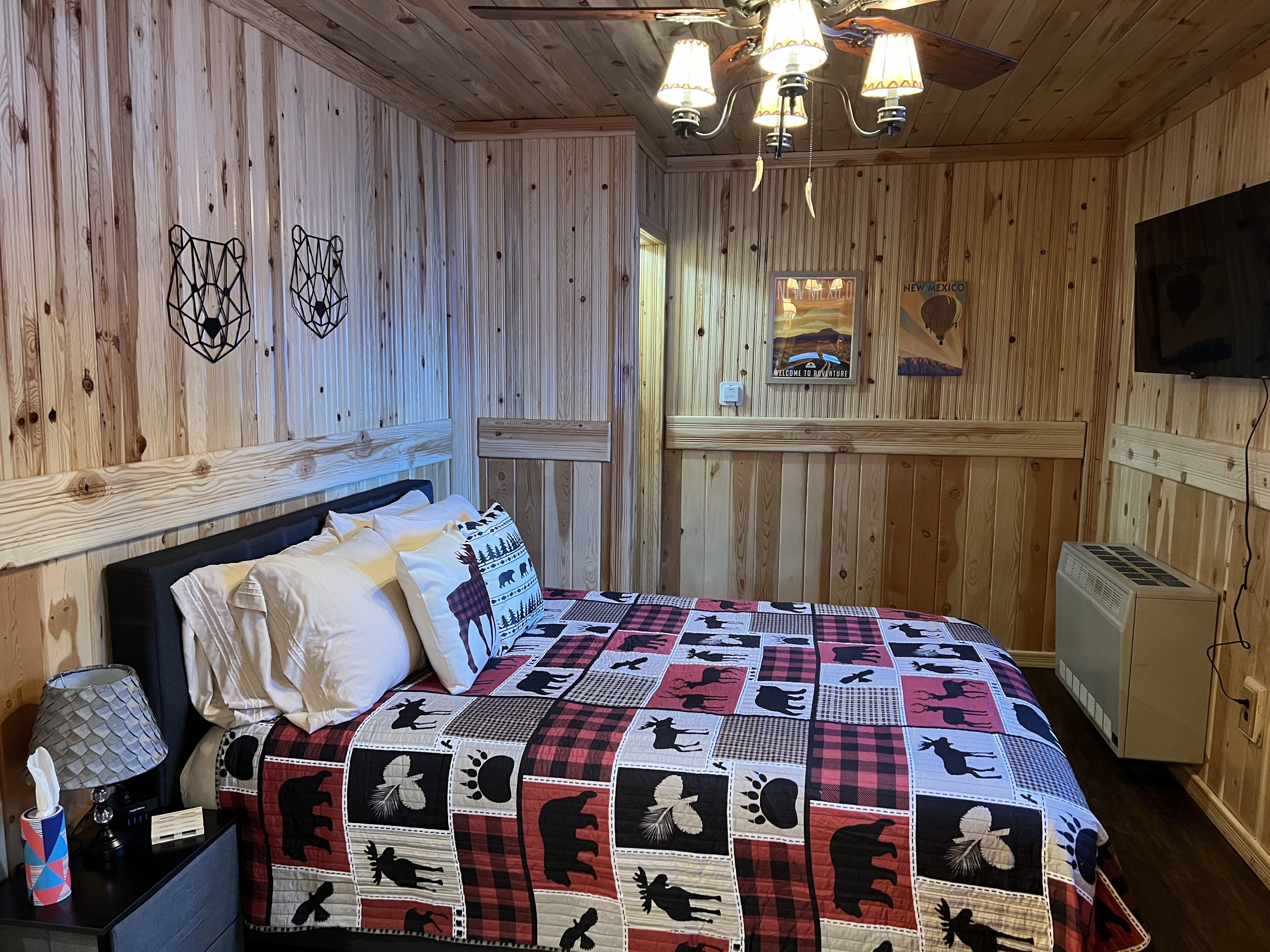 Una habitación acogedora con pared de madera, una cama con colcha, una mesita de noche, una lámpara y un calentador.