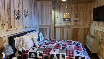 Una habitación acogedora con pared de madera, una cama con colcha, una mesita de noche, una lámpara y un calentador.