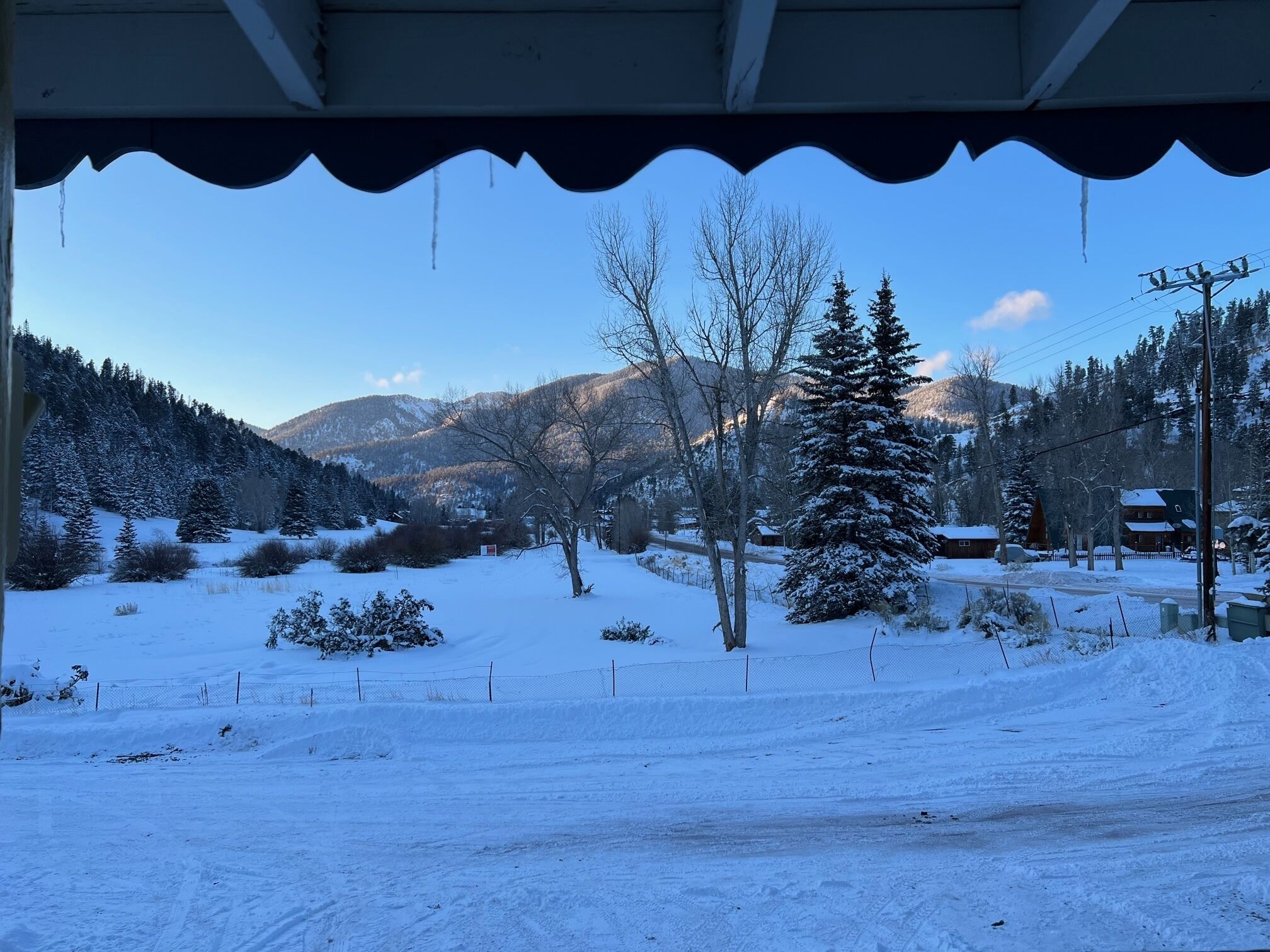 A snowy landscape with a clear view of a mountain range, a few trees, and a building in the distance.