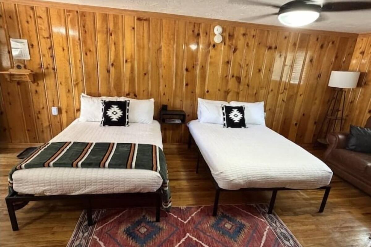Una habitación con dos camas, paredes de madera, un ventilador de techo y una alfombra estampada.