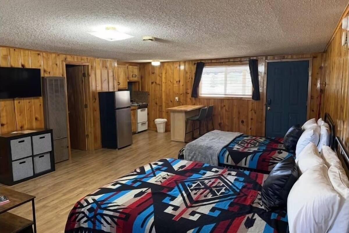 Una habitación compacta con cama, escritorio, kitchenette y televisor.