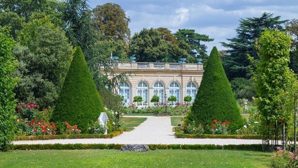 A formal garden with a symmetrical layout, featuring a central pathway leading to a building with arched windows and a balcony. - Superbe appart de 129m2, 3 ch-Neuilly 2 min Paris (Neuilly-sur-Seine)