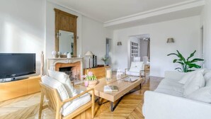 A modern living room with a fireplace, a television, a sofa, and a dining area. - Superbe appart de 129m2, 3 ch-Neuilly 2 min Paris (Neuilly-sur-Seine)