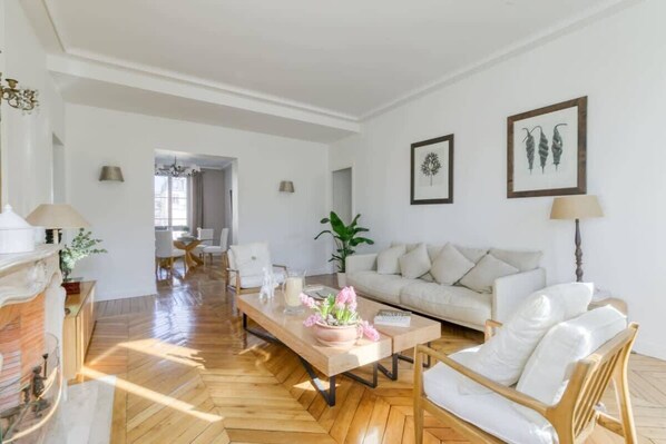 A spacious living room with a herringbone floor, a sofa, a coffee table with flowers, and a fireplace.