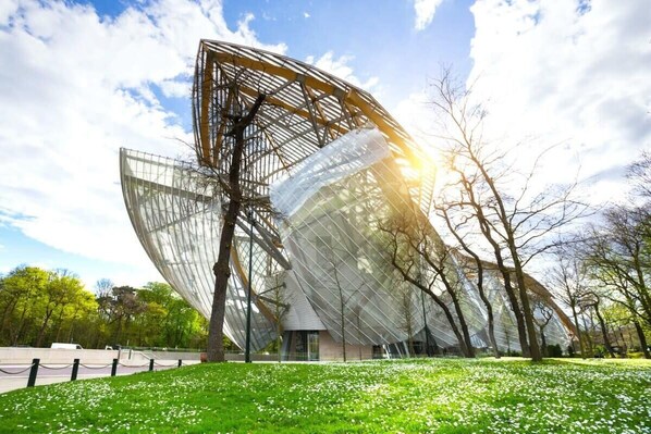 A modern architectural building with a unique, angular design, surrounded by a grassy area with trees. - Superbe appart de 129m2, 3 ch-Neuilly 2 min Paris (Neuilly-sur-Seine)