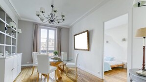 A modern room with a dining table, chairs, a chandelier, a bed, and a large window. - Superbe appart de 129m2, 3 ch-Neuilly 2 min Paris (Neuilly-sur-Seine)