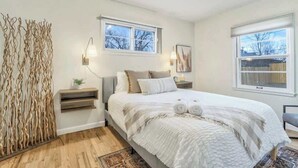 Quarto com uma cama grande, duas mesas de cabeceira, uma luminária na parede e uma janela com vista para árvores.