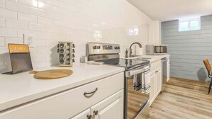 A kitchen with white tiles, a microwave, a toaster, and a wooden cutting board. - El Sereno Bungalow! Pet-Friendly Ivywild Flat (Colorado Springs)