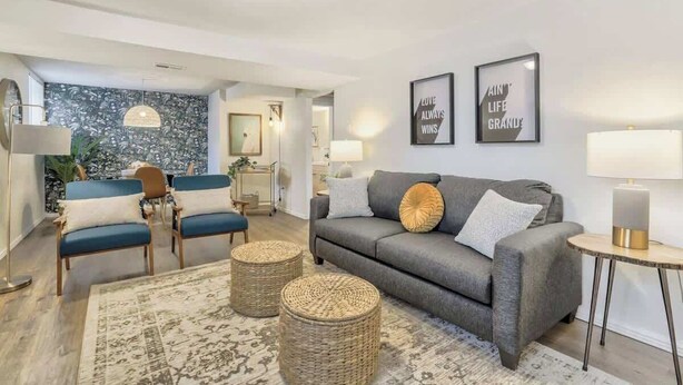 A living room with a grey sofa, blue chairs, a patterned rug, and two wall-mounted lamps. - El Sereno Bungalow! Pet-Friendly Ivywild Flat (Colorado Springs)