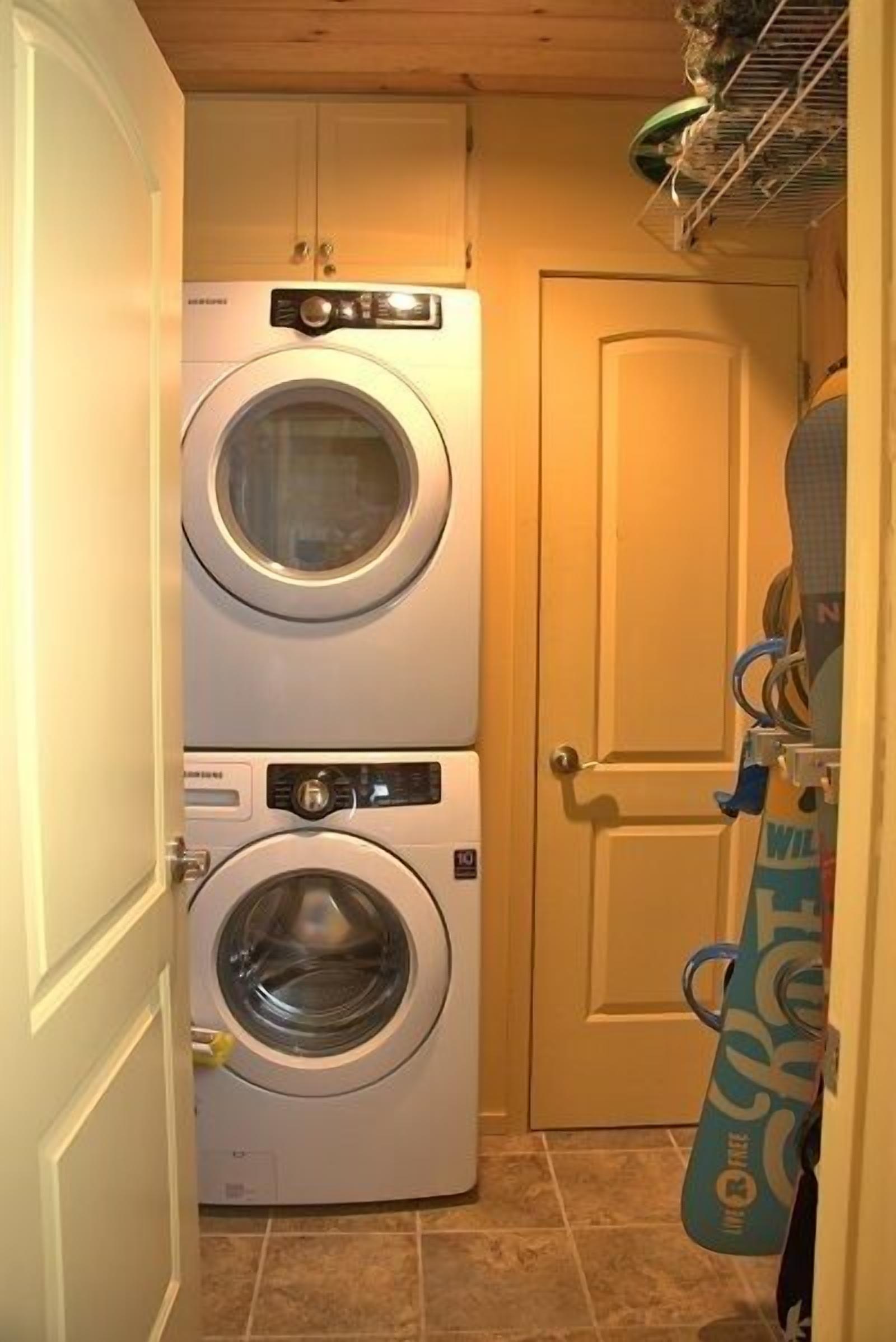 A laundry room with two stacked front-loading washing machines and a door to a storage area.