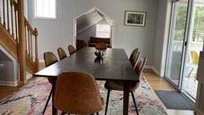 Ein Essbereich mit einem langen Tisch, mehreren Stühlen, einer Schüssel und einem farbenfrohen Teppich.