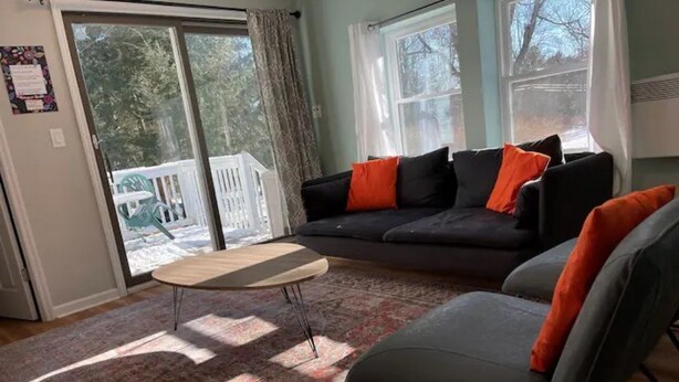Ein Wohnzimmer mit einer Couch, einem Sessel, einem Couchtisch und Blick auf eine Terrasse durch eine Schiebetür.