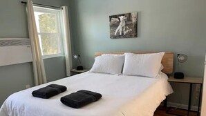 Ein Schlafzimmer mit einem großen Bett, zwei Nachttischen, einem Fenster und einem Wandbild.