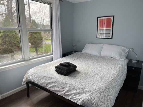 A bedroom with a bed, a nightstand, a lamp, and a window with curtains.
