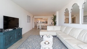 Una sala de estar moderna con un televisor de pantalla plana grande, un sofá de cuero blanco y un comedor al fondo.