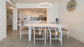 Una cocina moderna con armarios blancos, una isla central y una zona de comedor con una mesa y sillas blancas.