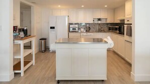Una cocina moderna con gabinetes blancos, una isla de acero inoxidable y un horno empotrado.