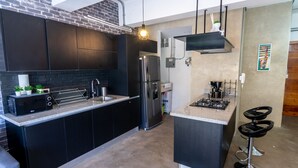 A modern kitchen with dark cabinetry, a stainless steel refrigerator, and a central island with bar stools. - New Loft NYC style, King Bed, High Speed Wifi, (Santo Domingo)
