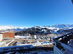 Ein verschneiter Bergort mit Parkplatz, Gebäuden und Blick auf schneebedeckte Berge.