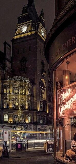 A historic building with a clock tower, illuminated by string lights, and a restaurant with a neon sign. - Captivating Apartment in Glasgow Westend, uk (Glasgow)
