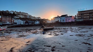 A coastal scene with a boat on a sandy beach, buildings in the background, and a sunset.