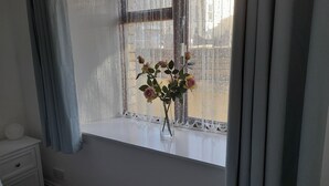 A bedroom with a window, a bedside table, and a vase with flowers. - Cosy Apartment Close to Tunnels Beaches (Ilfracombe)
