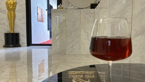 Ein Glas Rotwein auf einer spiegelnden Oberfläche mit einem Schild für das Lisbon City Hollywood Hotel.