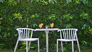Ein Garten mit einer Neonreklame mit der Aufschrift 'Hollywood City of Stars' und zwei weißen Stühlen an einem Tisch.