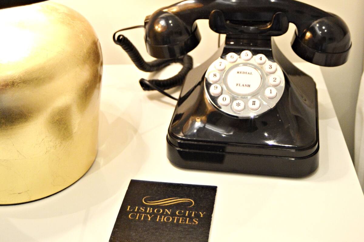 Ein schwarzes Wählscheibentelefon, eine goldene Lampe und ein Schild für das Lisbon City Hotel.