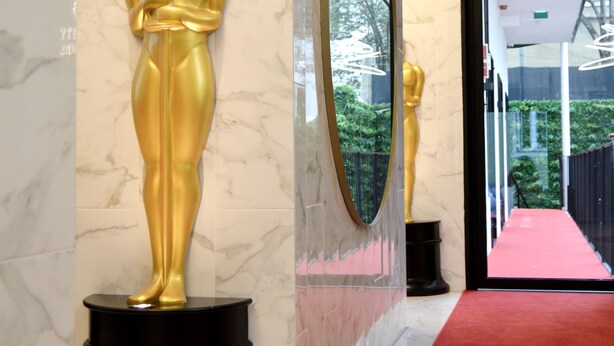 Eine Marmorwand mit einer goldfarbenen Statue einer Person, einem großen Spiegel und einem roten Teppich, der zu einer Tür führt.