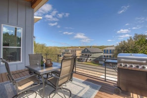 A deck with a table and chairs, a grill, and a view of houses in the background. - Lake-Pool-Beach-Gym-Boat Access (Lago Vista)