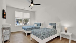 Ein Schlafzimmer mit zwei Betten, einem Deckenventilator, einem Fenster und einem Nachttisch mit einer Lampe.