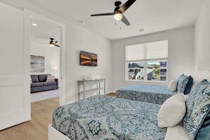 A bedroom with two beds, a ceiling fan, a window with blinds, and a painting on the wall.