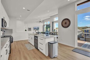 A modern kitchen with white cabinetry, a central island, and a large window offering a view of the outdoors. - Lake-Pool-Beach-Gym-Boat Access (Lago Vista)