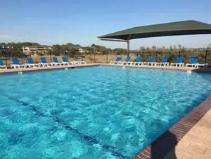 A swimming pool with clear blue water, surrounded by lounge chairs and a shaded area.