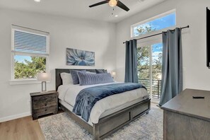 A bedroom with a bed, bedside tables, a ceiling fan, a window with blinds, a painting, and a view of the outdoors. - Lake-Pool-Beach-Gym-Boat Access (Lago Vista)