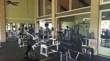 Un gimnasio con diferentes equipos de ejercicio, ventanas amplias y un ventilador de techo.