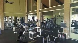 A gym with various exercise equipment, large windows, and a ceiling fan.