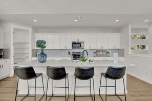 A modern kitchen with white cabinets, a central island with bar stools, and a microwave.