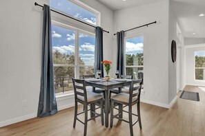 A dining area with a table set for four, large windows with curtains, and a view of the outdoors.