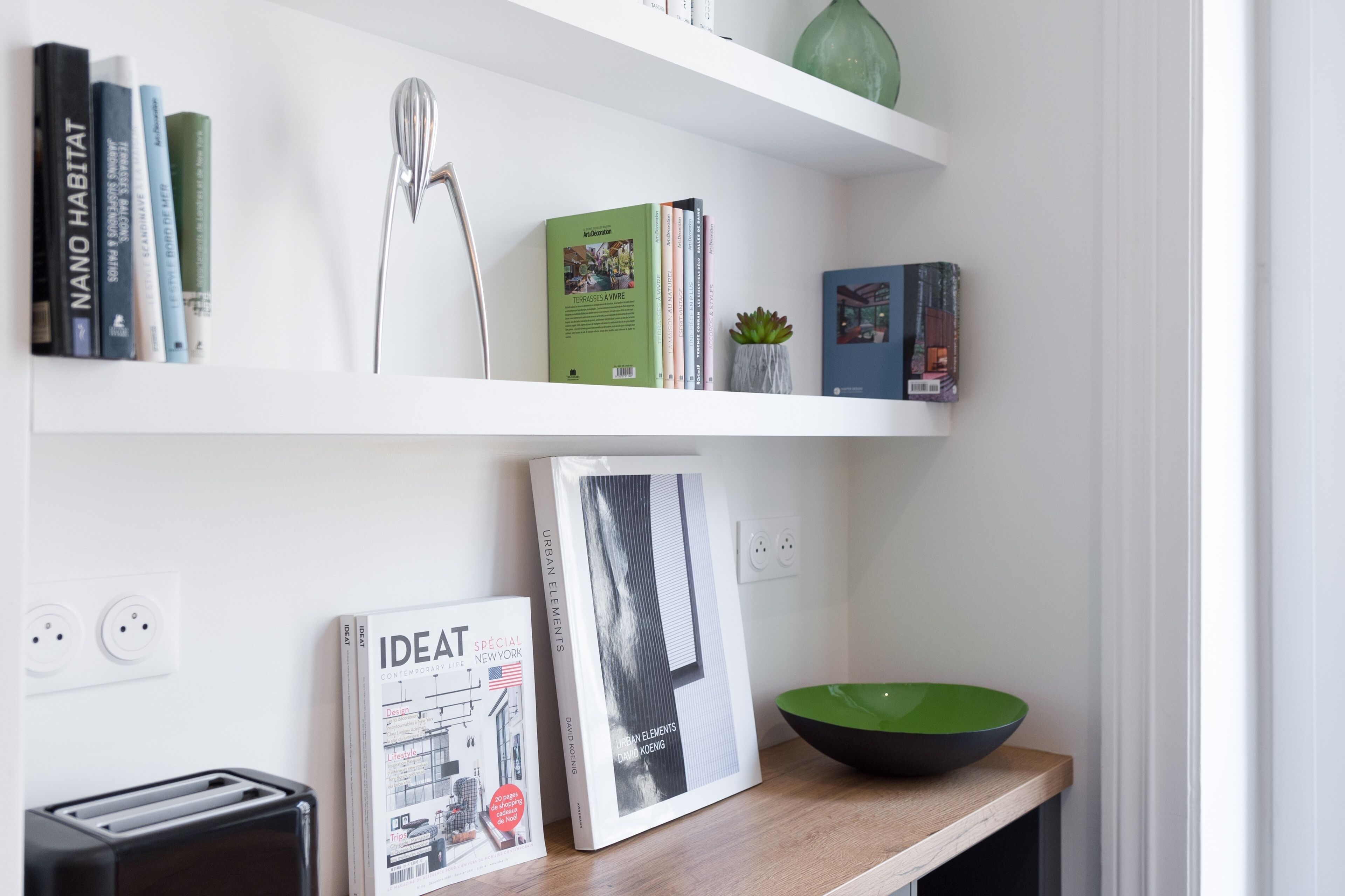 A clean, modern kitchen with white shelves, a green bowl, and books.