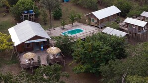 Una cabaña con piscina, terraza de madera y sombrillas de paja.